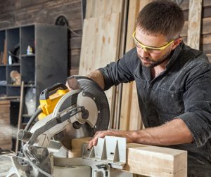 young man in safety goggles using a power saw to cut timbers