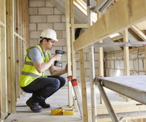 man using a drill on framed house walls