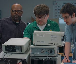 Instructor Wesley Williams guiding two students through using electrical device