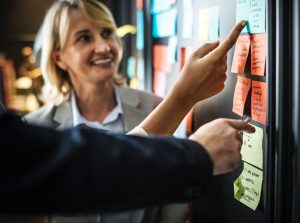 smiling lady using post it notes to help a gentleman with planning