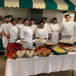 Group of culinary students posing behind a beautiful spread of food