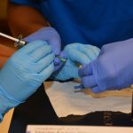 Close up of Pharmacy Tech student's hands, wearing latex gloves, working with a syringe