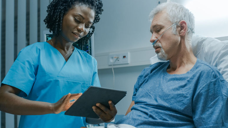 Nurse aide holding an electronic tablet at the bedside of a patient.