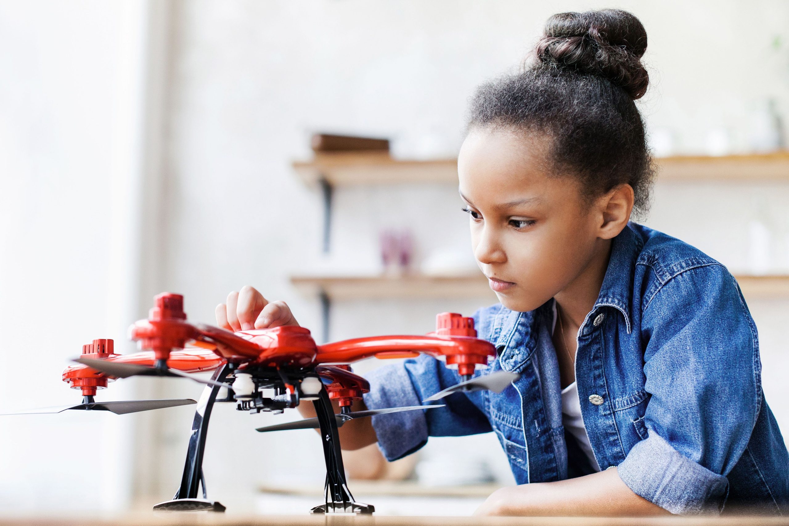 Young girl examining a red drone that is sitting on a table.